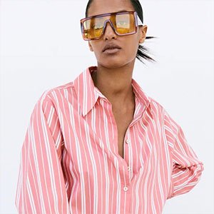 Pessoa usando camisa listrada em tons de rosa e branco e óculos de sol com lentes coloridas, em retrato de estilo editorial sobre fundo claro.