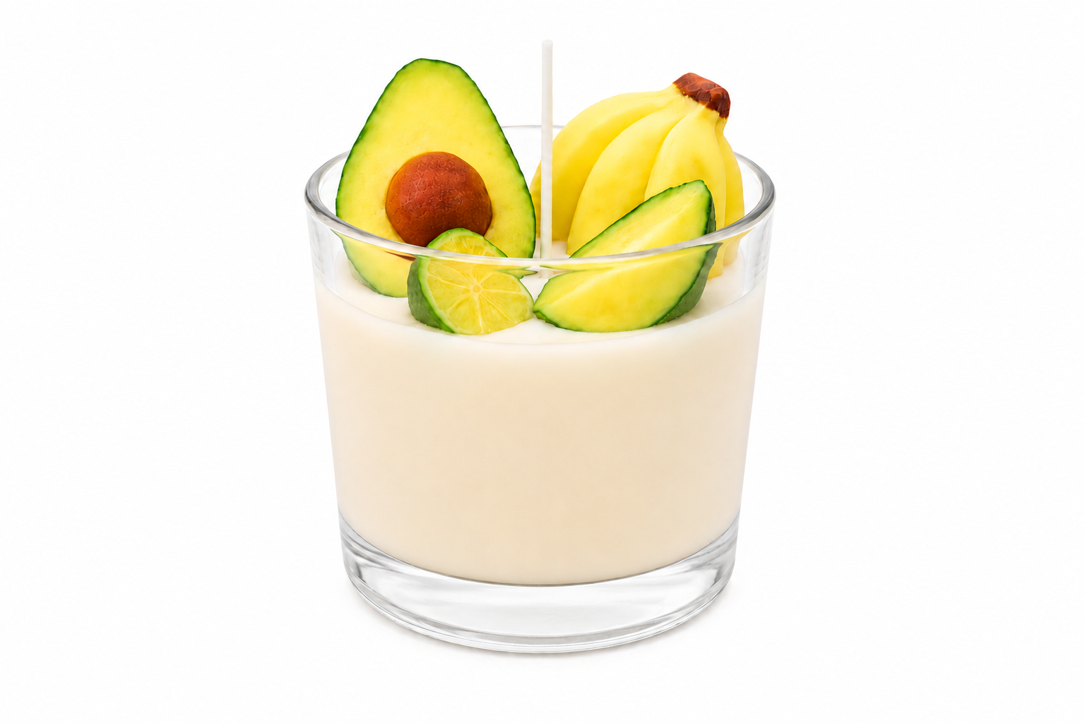 Vela Aromática de Frutas Tropicais em copo de vidro transparente, com cera cremosa em tom claro e decoração inspirada em frutas tropicais. A composição apresenta miniaturas de abacate, banana e limão sobre a superfície da vela, criando um visual alegre, colorido e artesanal. A imagem possui fundo branco e iluminação suave que destaca os detalhes decorativos.